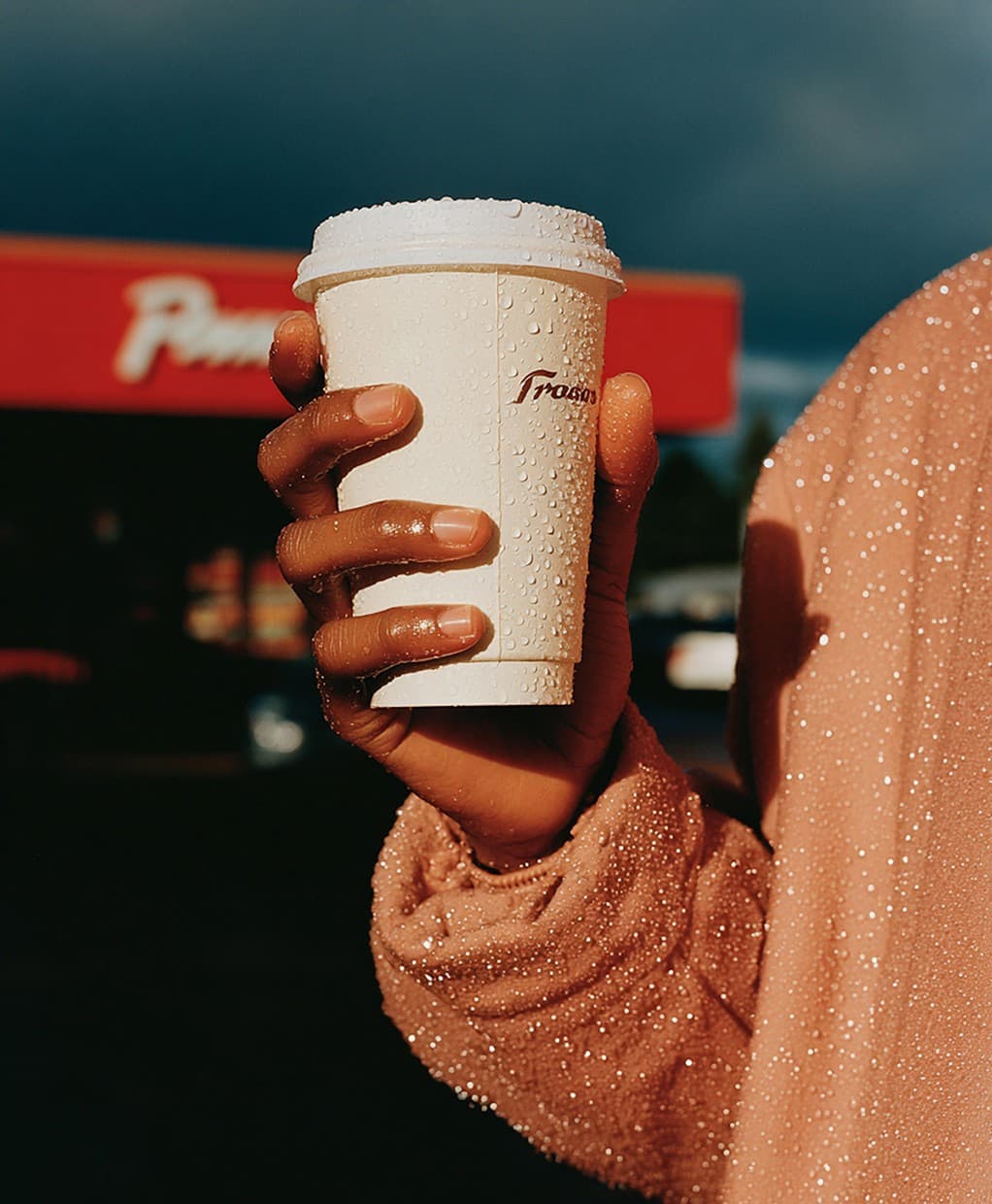 Hand holding a dewy coffee cup in front of a red storefront